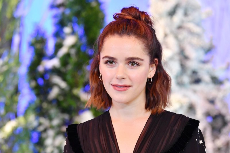 Kiernan Shipka smiles at the camera with auburn hair in a dark dress