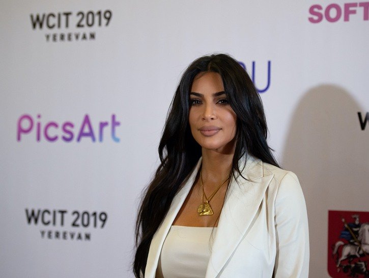 Kim Kardashian smiles in a white pantsuit against a white background