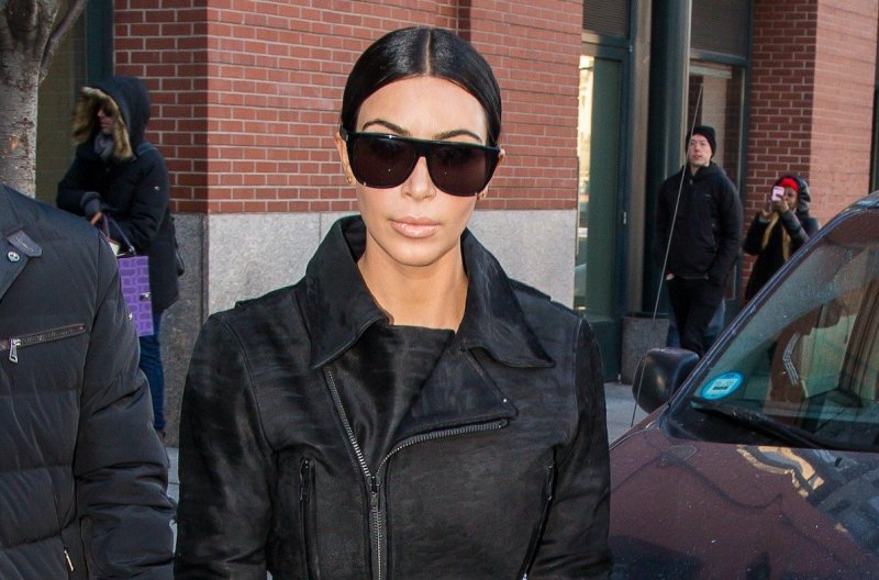 Kim Kardashian wearing black sunglasses and black jacket walking outside