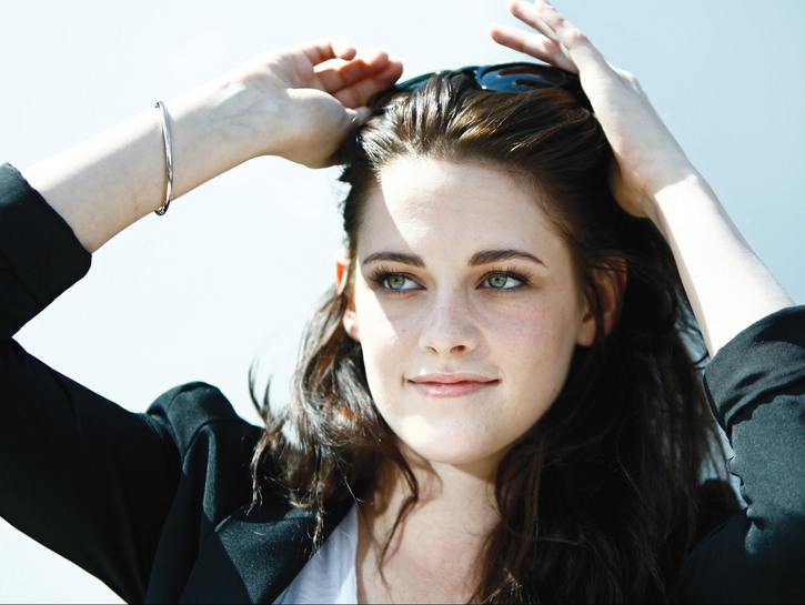 Kristen Stewart wearing a black blazer pushing her sunglasses up while at the Cannes Film Festival