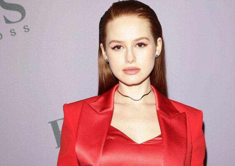 Madelaine Petsch looks at the camera in a red jacket and blouse against a light background at the BO