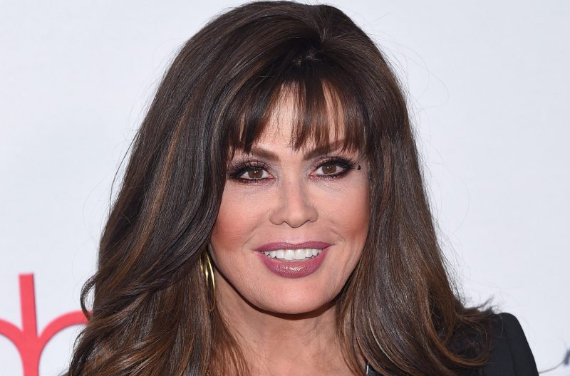 Marie Osmond wears a red dress under a black jacket on the red carpet