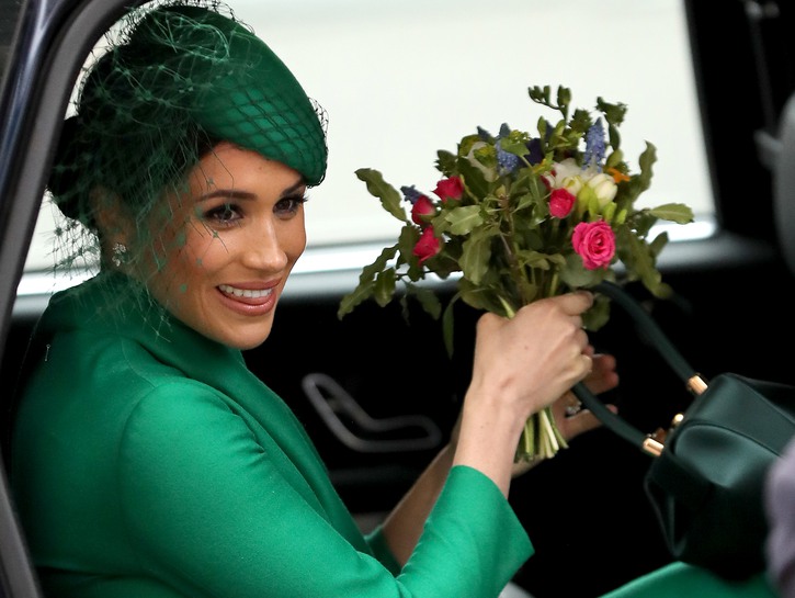 Meghan Markle riding in a car in a green dress with a bouquet of flowers in her hand