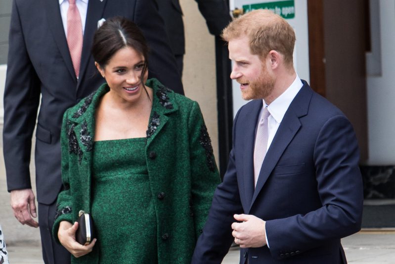 Meghan Markle wearing a green dress and coat walking with her husband Prince Harry, in a navy suit
