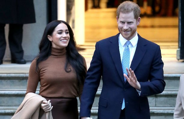 Meghan Markle wears a bron turtleneck and a brown skirt, Prince Harry wears a navy suit and a bright