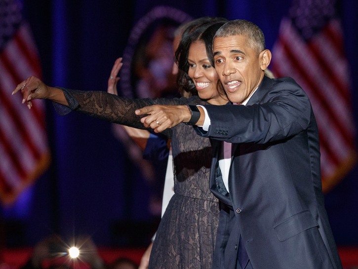 Michelle and Barack Obama pointing at something off-camera, together on stage at a campaign event.