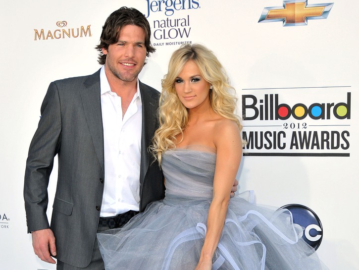 Mike Fisher, in a gray suit, stands with Carrie Underwood, in a gray and blue dress