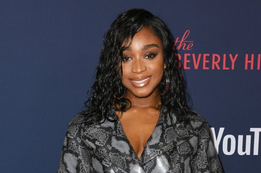 Normani smiles in a grey snakeskin jacket with her hair in curls