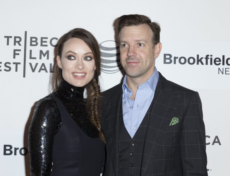 Olivia Wilde and Jason Sudeikis, both dressed in black, pose before a white background