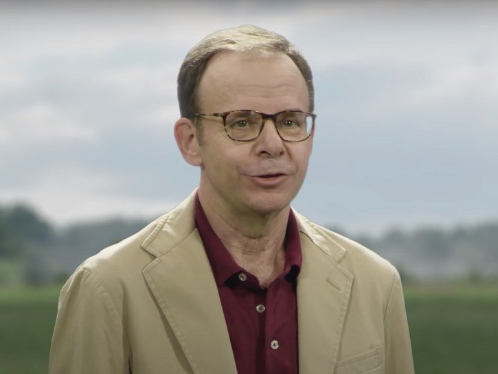 Rick Moranis wearing a tan blazer during a Mint Mobile commercial