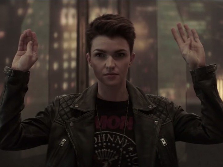 Ruby Rose in a leather jacket and black shirt holds her hands up in a scene from The CW's Batwoman s