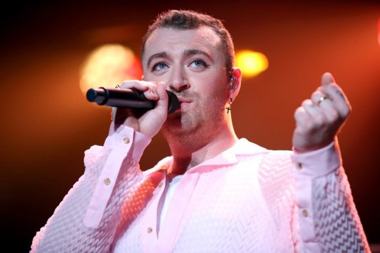Sam Smith sings into a microphone in a pink ruffled shirt