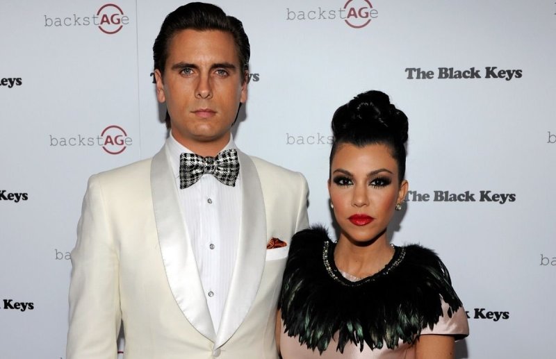 Scott Disick in a white suit standing with Kourtney Kardashian, who's wearing a pink dress with a bl