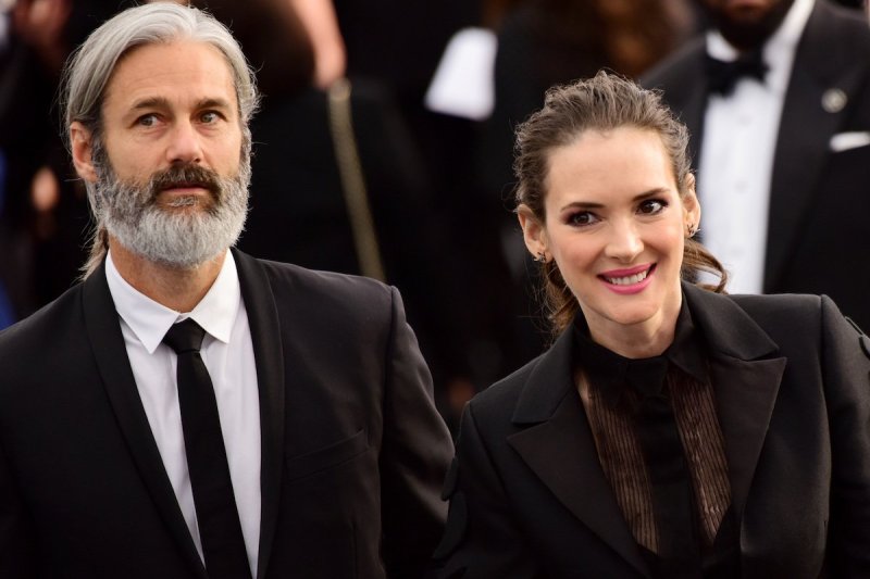 Scott Mackinlay Hahn in a black suit and tie walking with smiling Winona Ryder in a black dress
