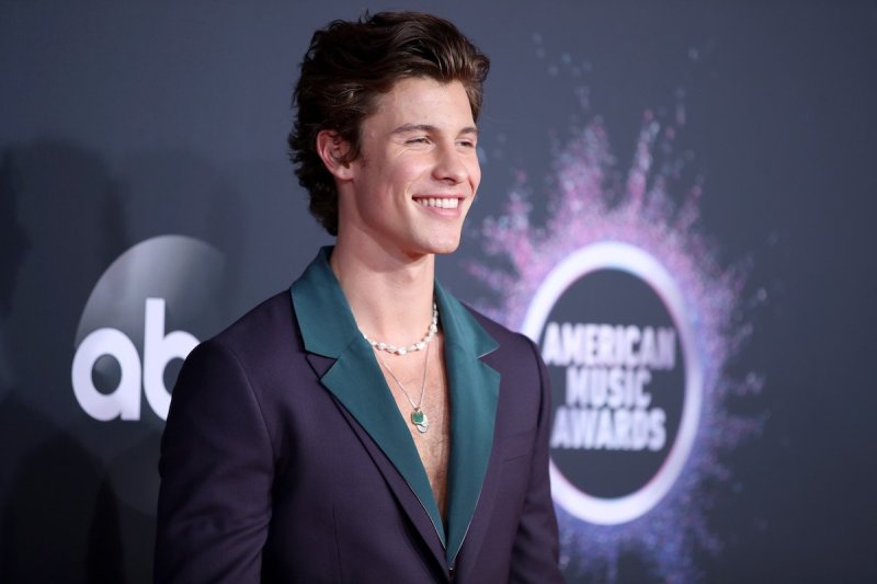 Shawn Mendes smiles to his left in a black jacket with a green collar