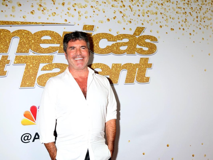 Simon Cowell smiling in a white button up shirt against a white background