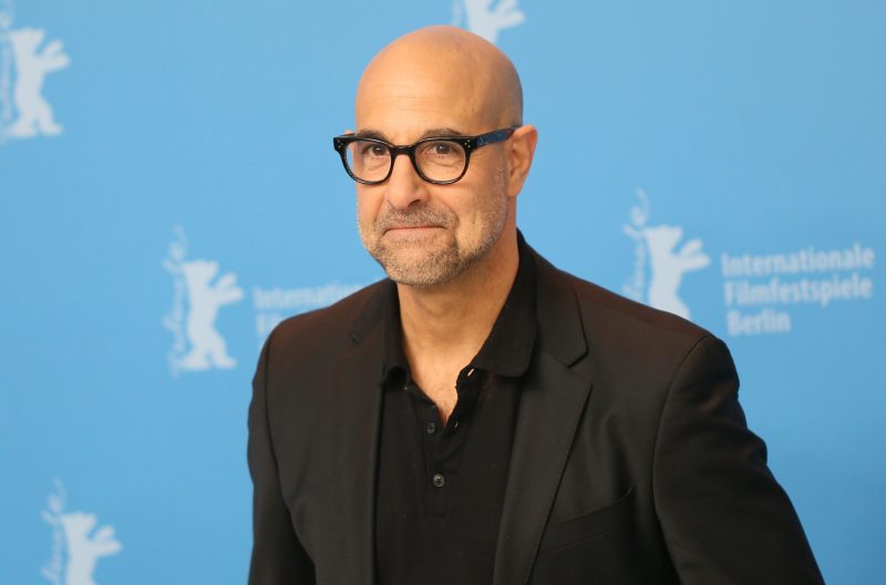 Stanley Tucci at the 67th Berlinale Film Festival in a black suit, black shirt with first few buttons undone, and glasses.