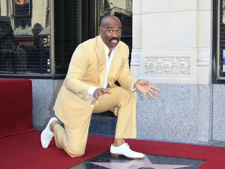 Steve Harvey smiles in a yellow suit while kneeling in front of his Hollywood Blvd star.