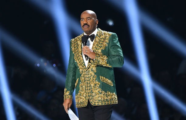 Steve Harvey wearing a green and gold suit jacket at the Miss Universe pageant