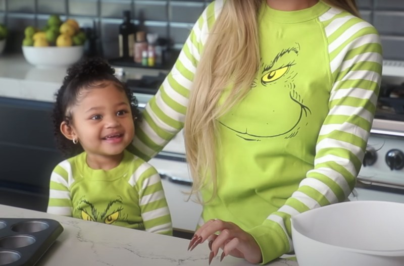 Stormi Webster stands by her mom, Kylie Jenner in their kitchen wearing matching Grinch pajamas