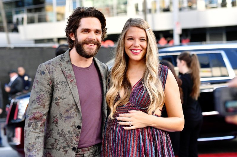 Thomas Rhett in a flower patterned suit with his arm around pregnant wife Lauren Akins