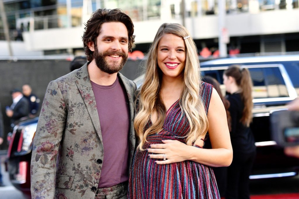 Thomas Rhett in a flower patterned suit with his arm around pregnant wife Lauren Akins