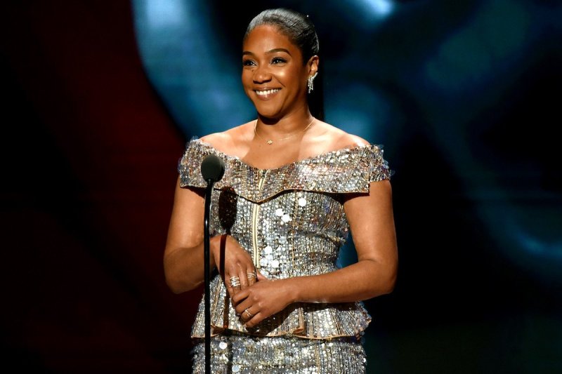 Tiffany Haddish smiles in a silver dress while standing at a mic at the BET Awards