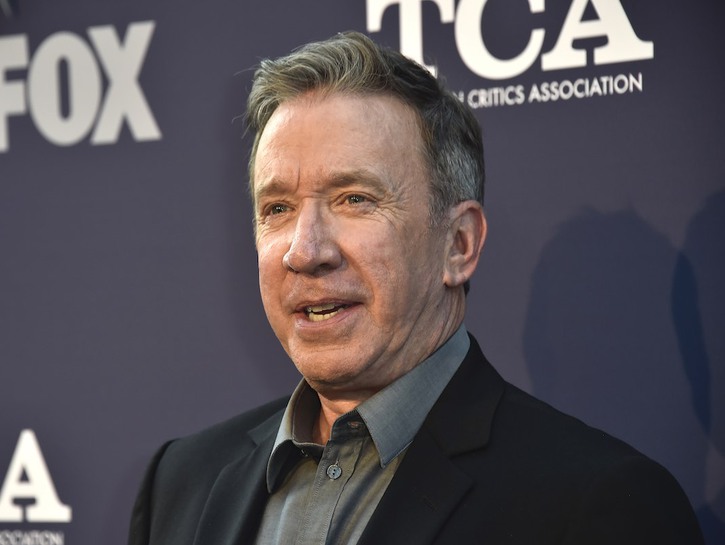 Tim Allen looks forward in a black suit against black background