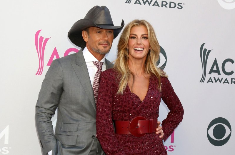 Tim McGraw, in a gray suit and cowboy hat poses with wife Faith Hill, in a red leopard print dress