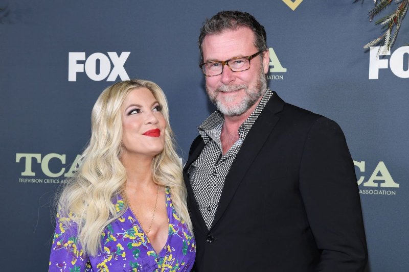 Tori Spelling in a purple dress smiles and looks up at Dean McDermott in a black and grey suit