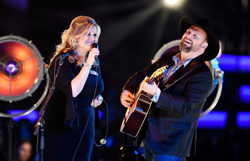 Trisha Yearwood in a black dress and Garth Brooks in a black suit jacket on stage at MusiCares