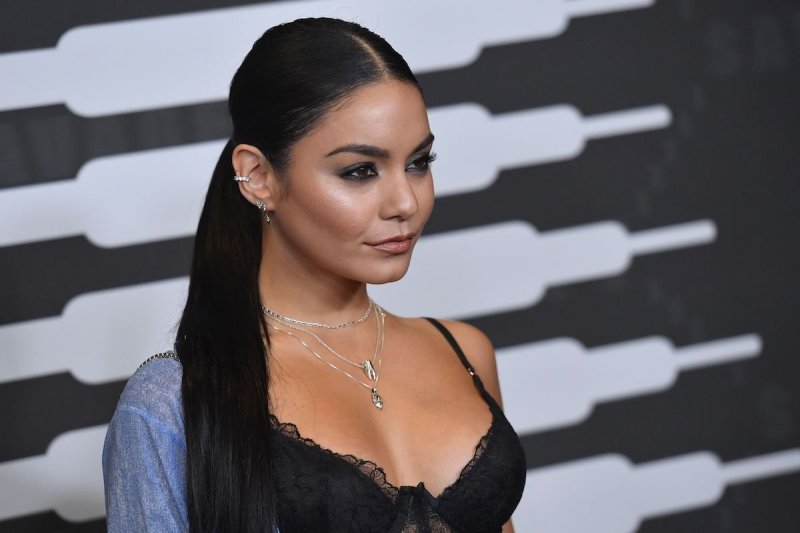 Vanessa Hudgens smiles off camera in a loose blue shirt on one shoulder and a black lacy top
