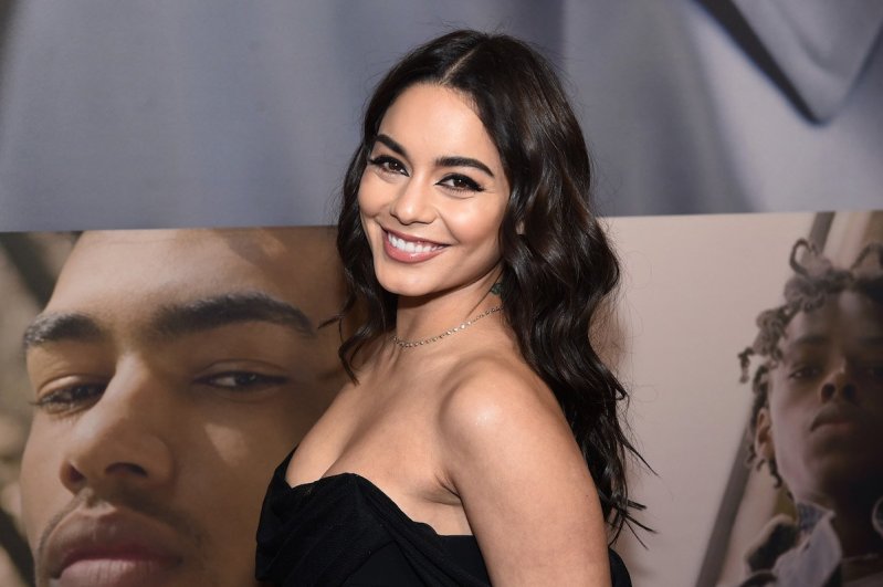 Vanessa Hudgens turns and smiles at the camera in a black dress at the West Side Story opening