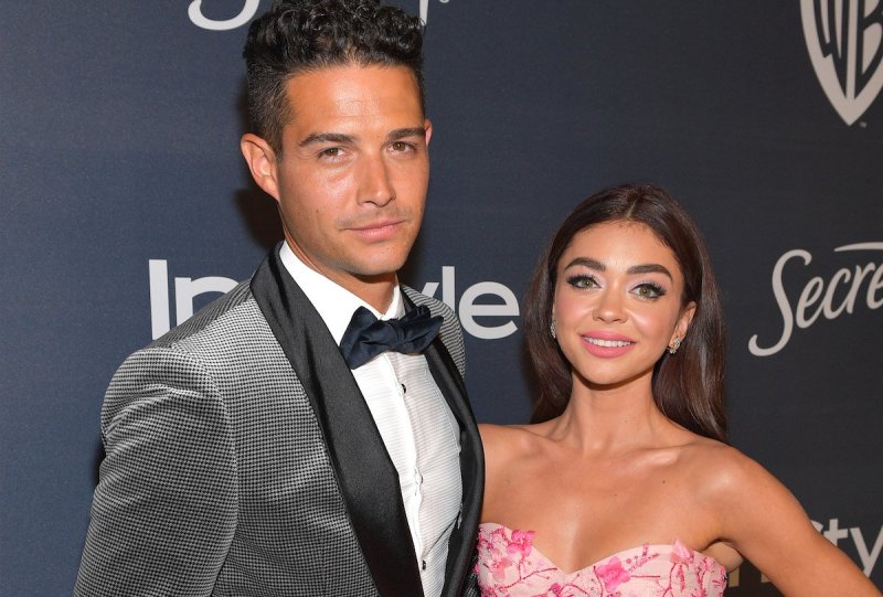 Wells Adams in a grey tux with his arm around Sarah Hyland in a pink dress