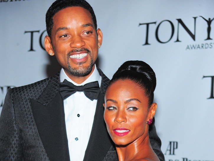 Will Smith wearing a black tux standing with his wife, Jada Pinkett, at a red carpet event.