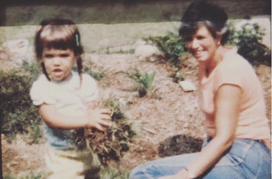 A photo of Katie Holmes as a young girl playing in a garden with her mother