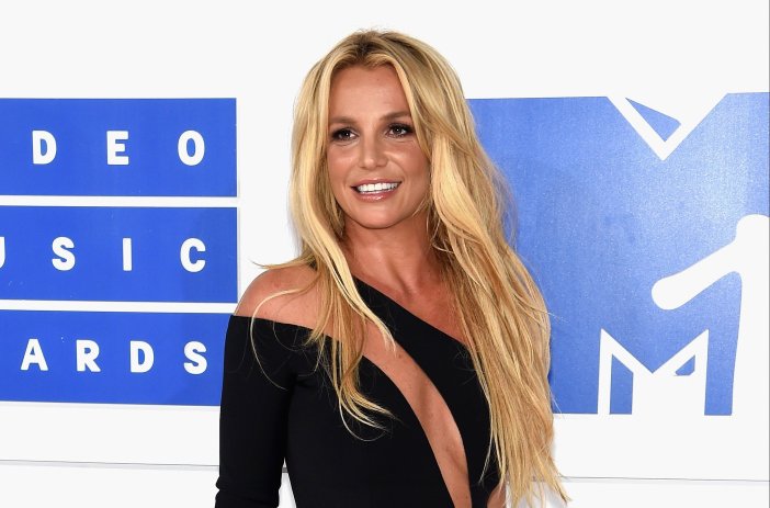 Britney Spears in front of a blue background, wearing a black dress.