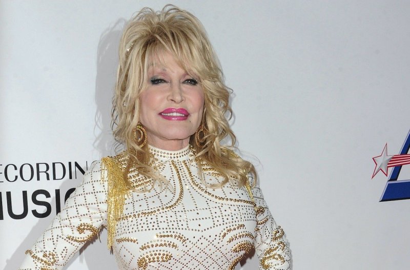 Dolly Parton smiling in a gold and white dress against a white background