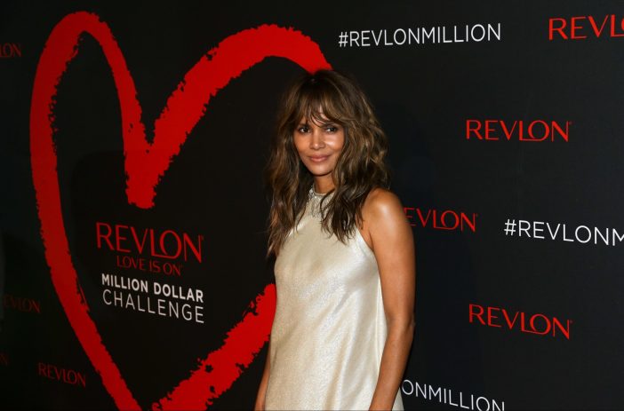 Halle Berry wears an ivory sheath dress as she stands in front of a black and red background