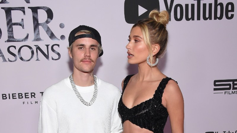 Justin Bieber, in white, stands with Hailey Baldwin, in a black two piece dress