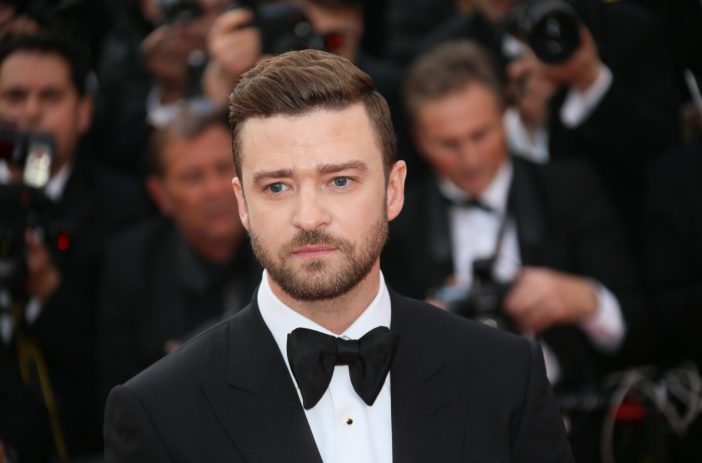 Justin Timberlake stands before photographers wearing a black tux on the red carpet