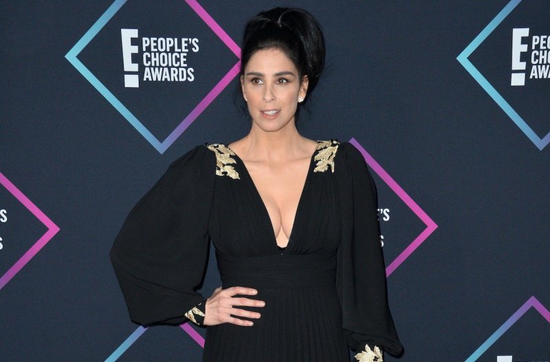 Sarah Silverman smiling in a black dress with hand on hip