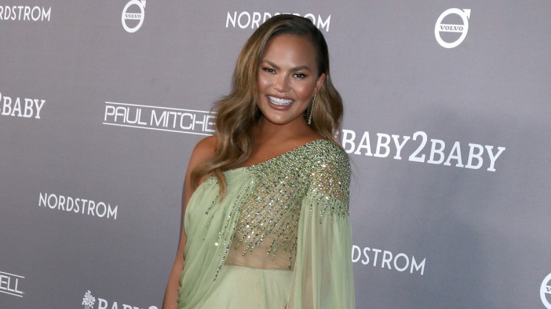 Chrissy Teigen smiling in a green dress