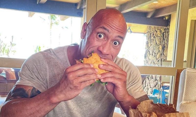 screenshot of Dwayne The Rock Johnson biting into a burger