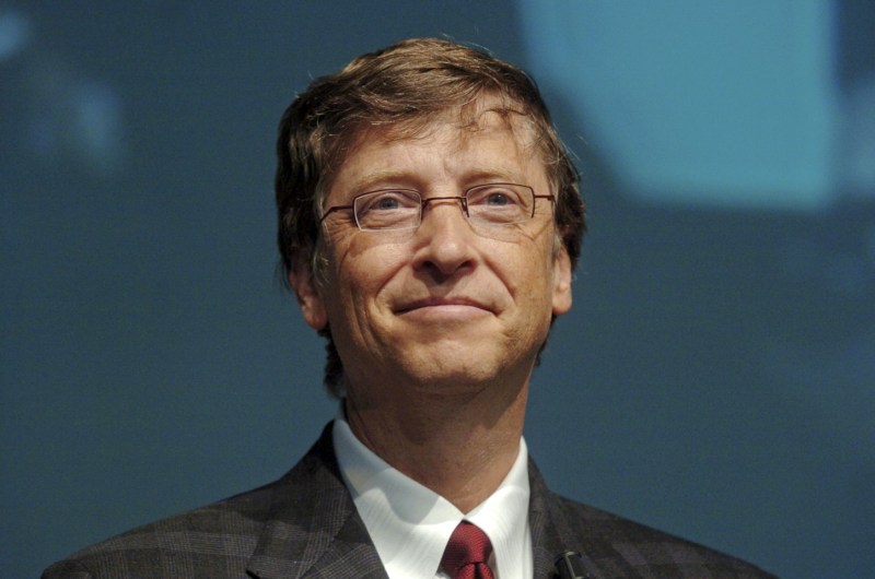 Bill Gates smiling and wearing a suit with a red tie.