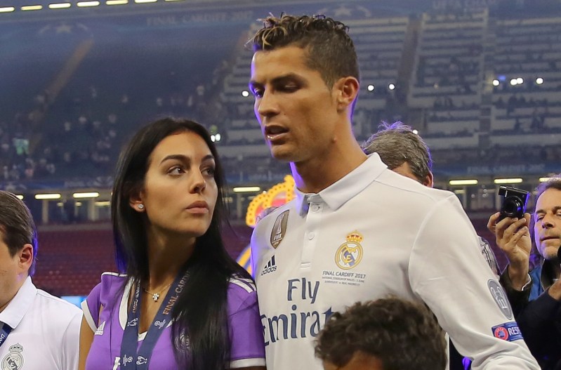 Cristiano Ronaldo wearing a soccer jersey stands with his girlfriend, Georgina Rodriguez, wearing a purple shirt.