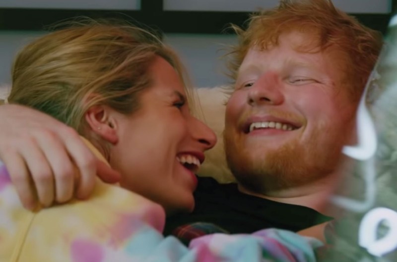 Ed Sheeran and his wife, Cherry Seaborn smiling and lying in each other's arms.