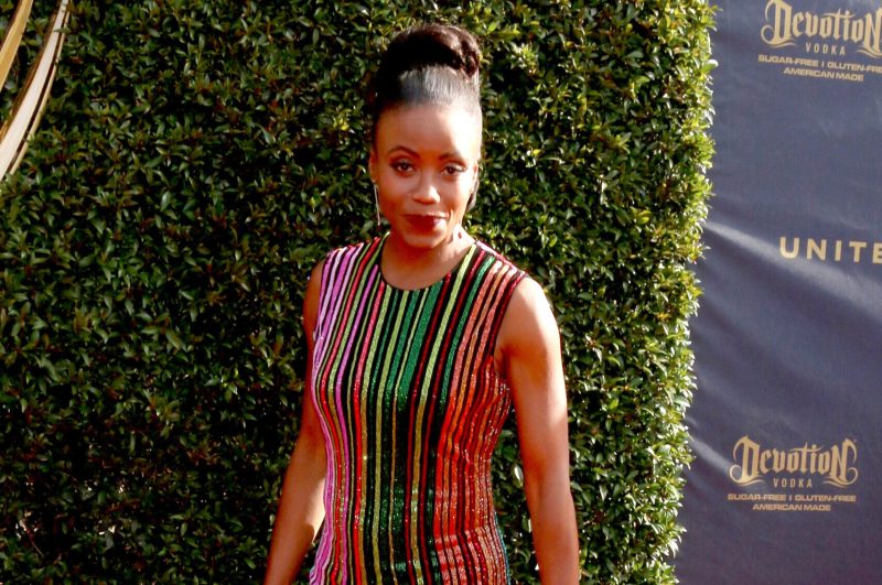Tanya Acker on a red carpet wearing a multicolored and striped dress.