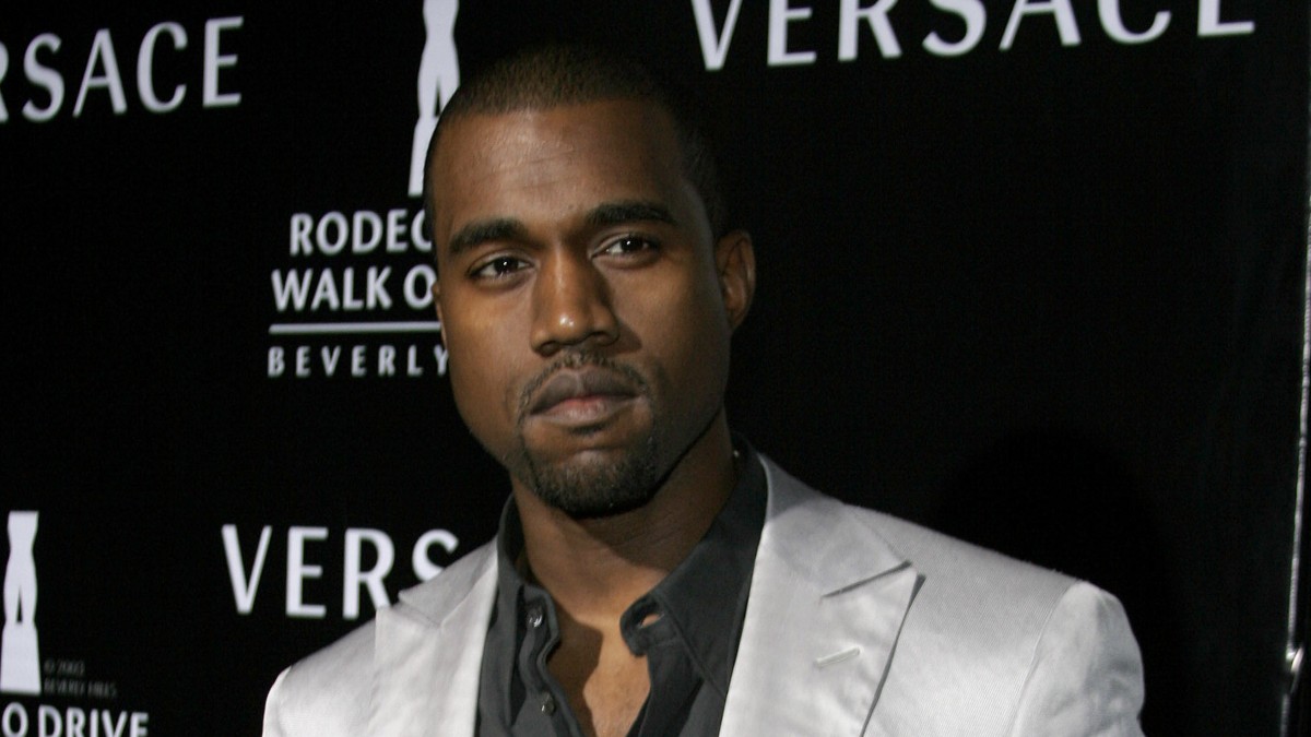 Kanye West wears a silver suit jacket against a black backdrop