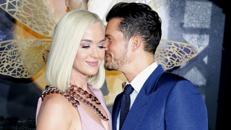 Katy Perry wearing a pink dress stands with Orlando Bloom, in a blue suit